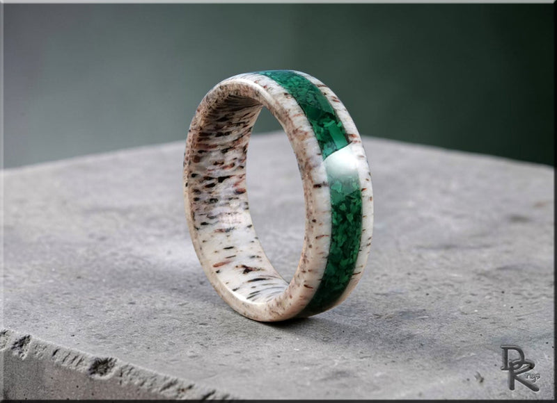 Close-up of a deer antler ring with a green inlay on a concrete surface