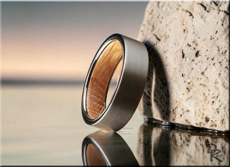 Close-up of a tungsten rings band with a brushed shell design and wood inlay on reflective surface