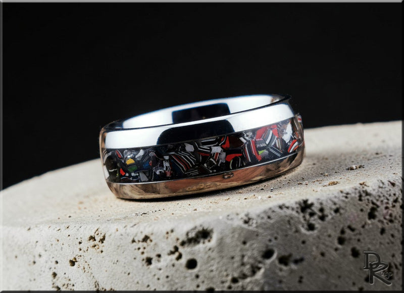 Close-up of a polished tungsten metal ring with colorful inlay design on a textured stone surface