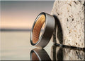 Gun metal tungsten ring with smooth matte finish and polished edges leaning against textured stone