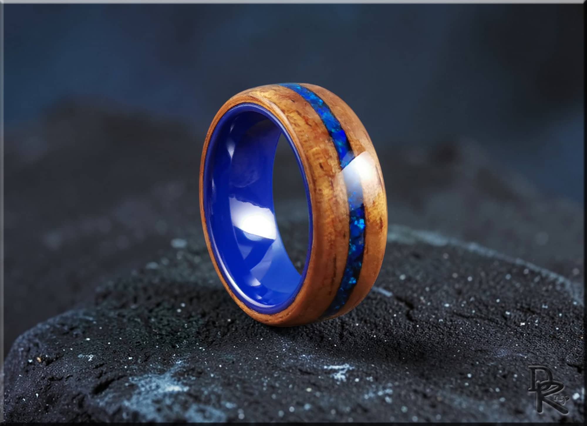 Koa wood ring with opal and ceramic blue inlay by DR Rings on black textured surface