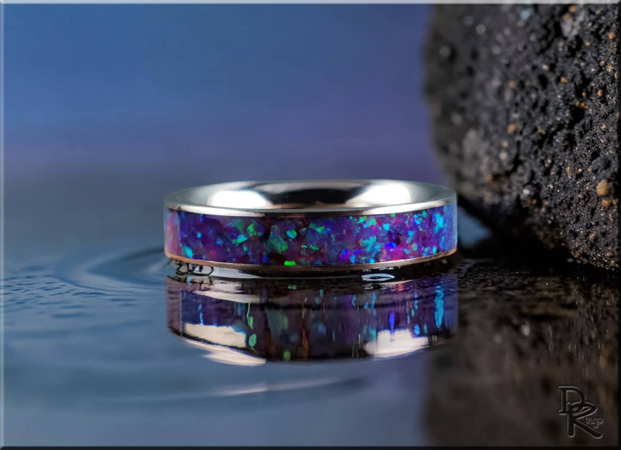 Narrow titanium ring with opal inlay featuring vibrant blue and green hues on a reflective surface