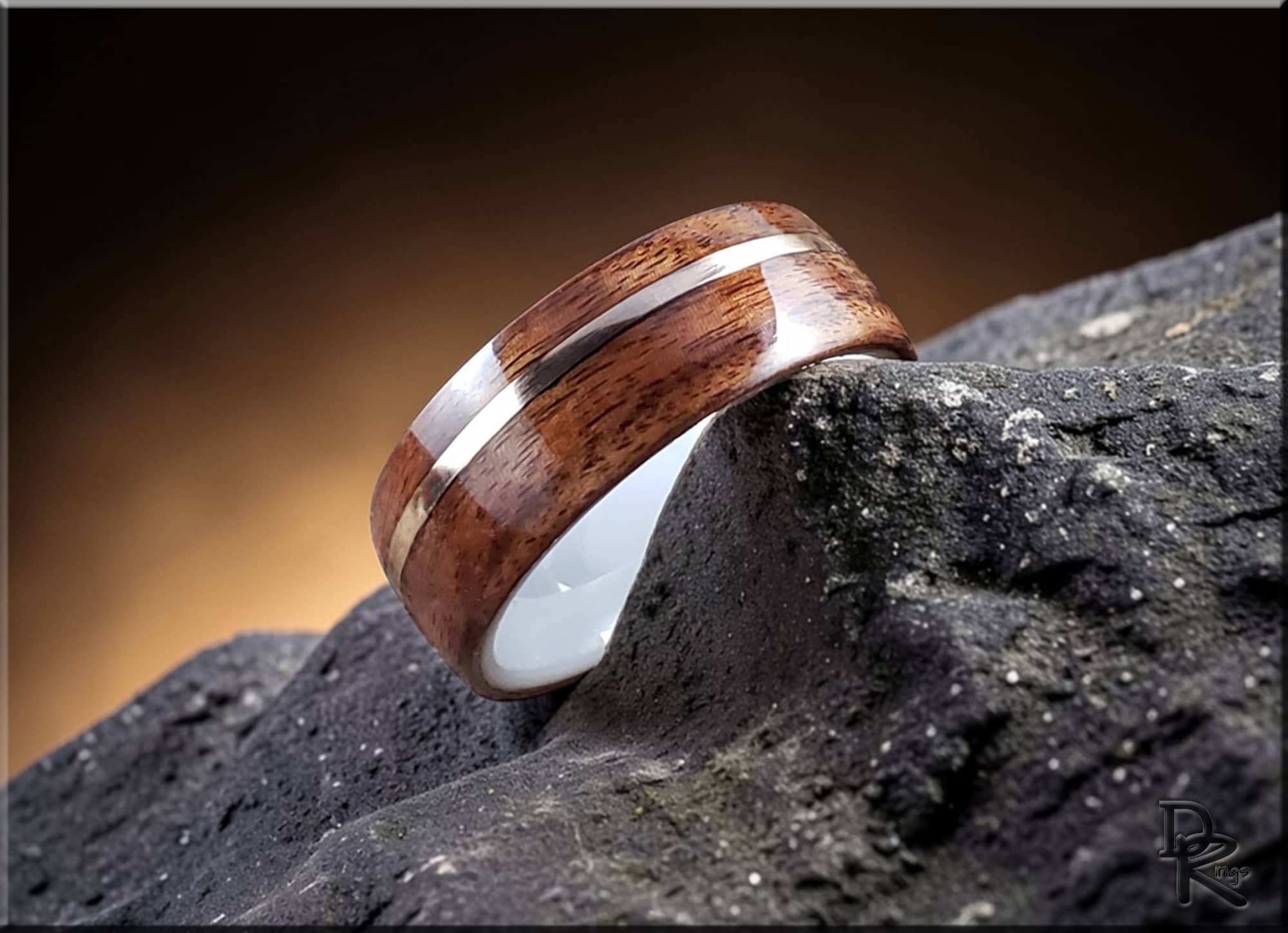 DR Rings rosewood ring with wire inlay placed on textured dark rock with warm background