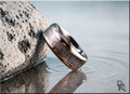 DR Rings titanium ring with inlay resting on rock by calm water with ripple reflections
