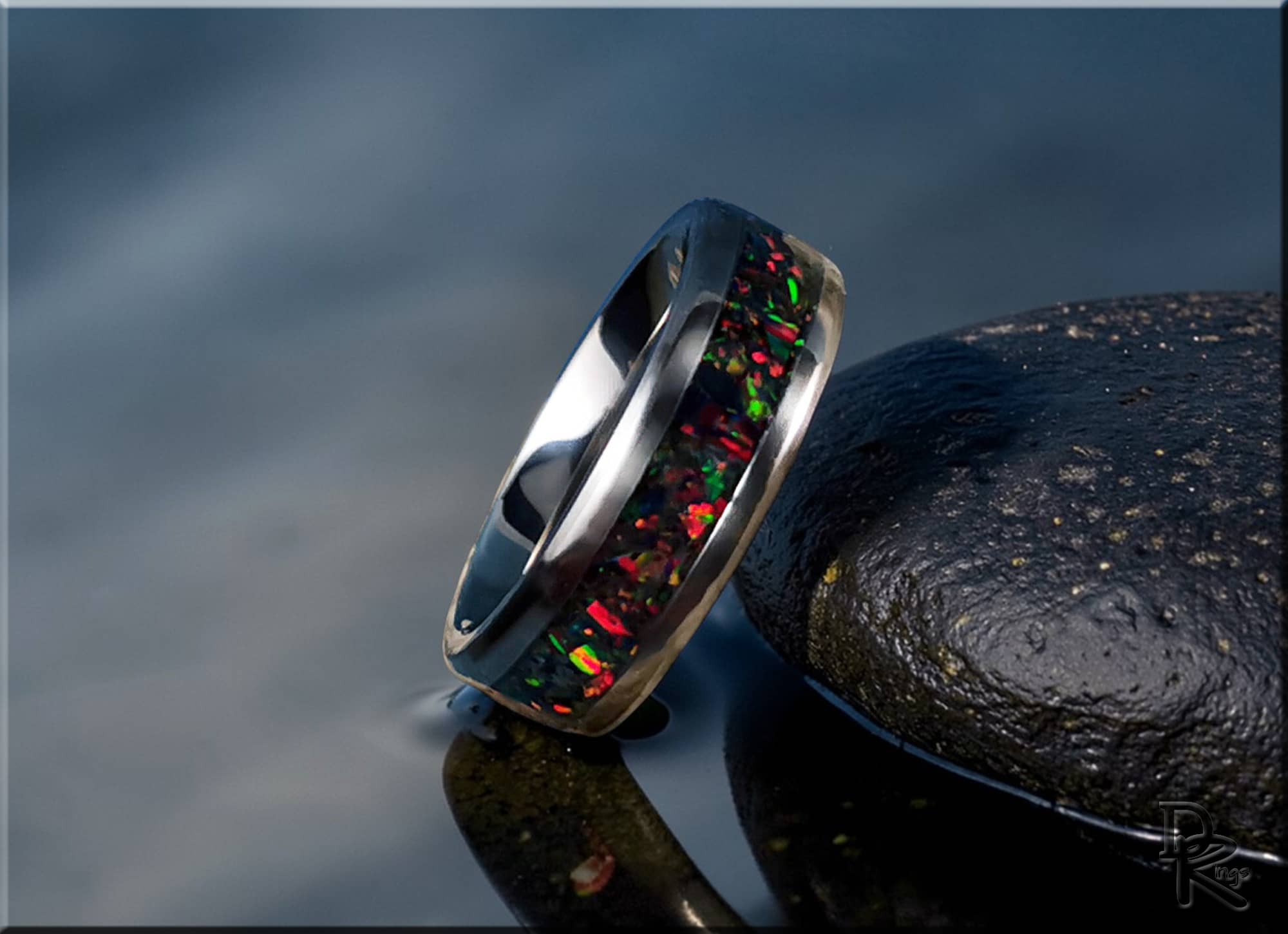 DR Rings titanium ring with opal inlay featuring vibrant red and green flashes on a reflective surface