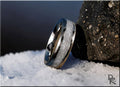 Titanium ring with selenite center band showcased on snowy surface next to volcanic rock