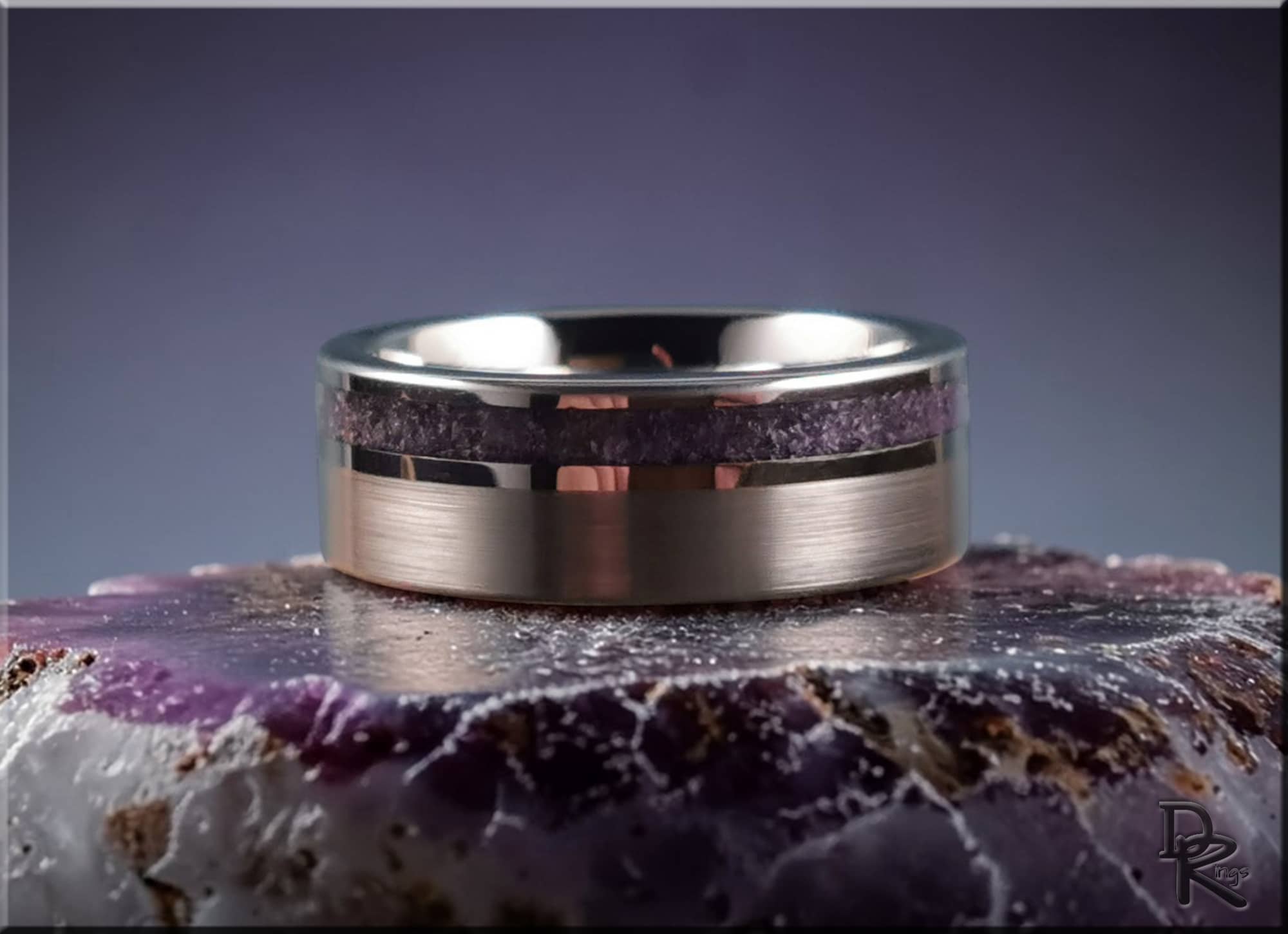 DR Rings tungsten ring with amethyst band resting on a purple agate stone