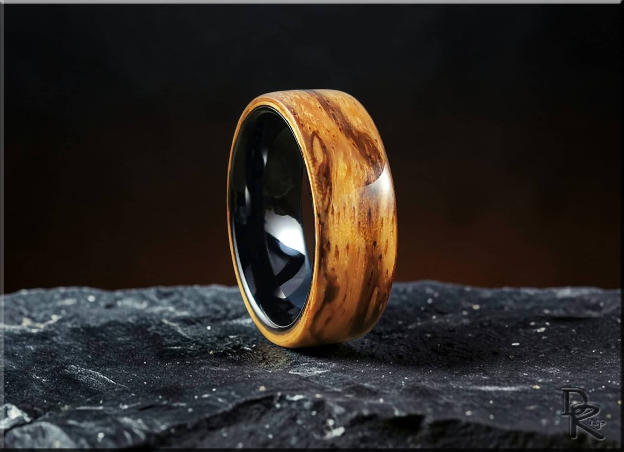 Elegant wood ring on ceramic core with smooth polished finish displayed on textured stone