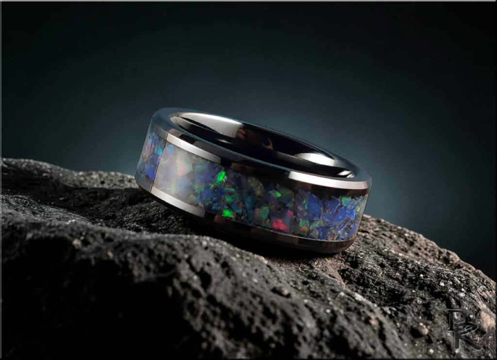 Black ceramic ring with opal inlay featuring vibrant blue and green flashes on textured black surface