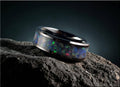 Black ceramic ring with opal inlay featuring vibrant blue and green flashes on textured black surface