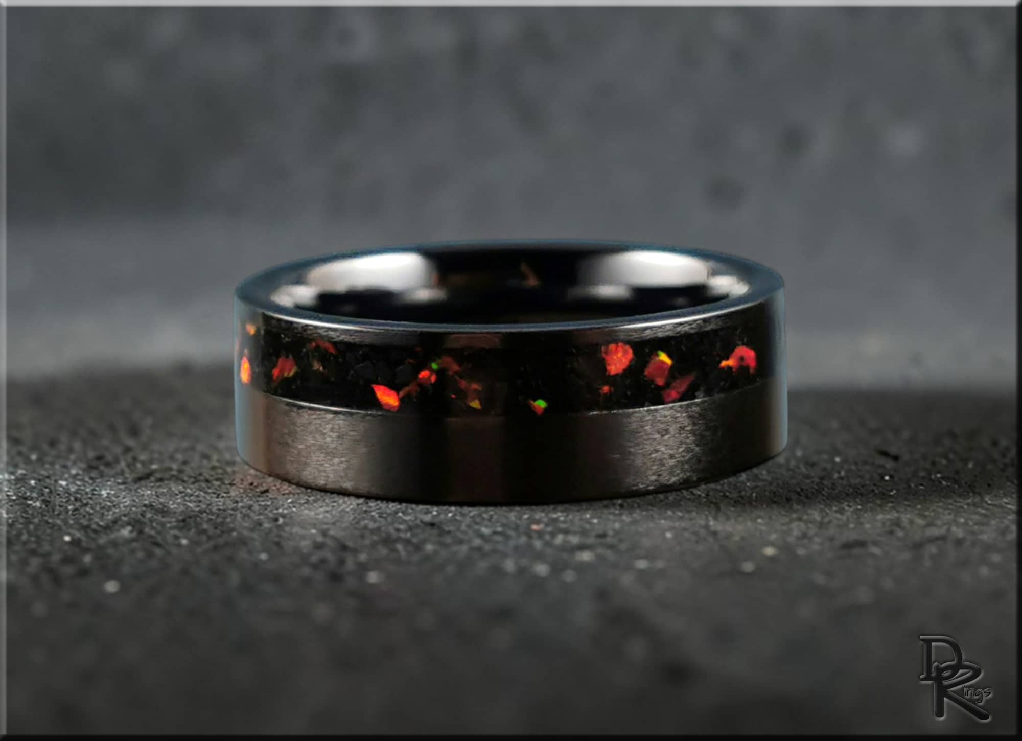 DR Rings black band ring opal inlay with vibrant red and orange flecks on dark textured surface