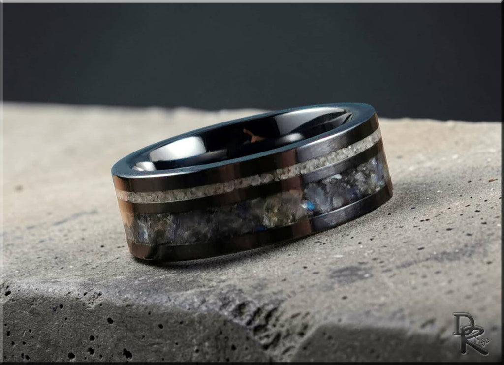 Black ceramic ring with dual inlays lying on textured stone surface by DR Rings