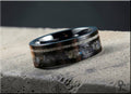 Black ceramic ring with dual inlays lying on textured stone surface by DR Rings