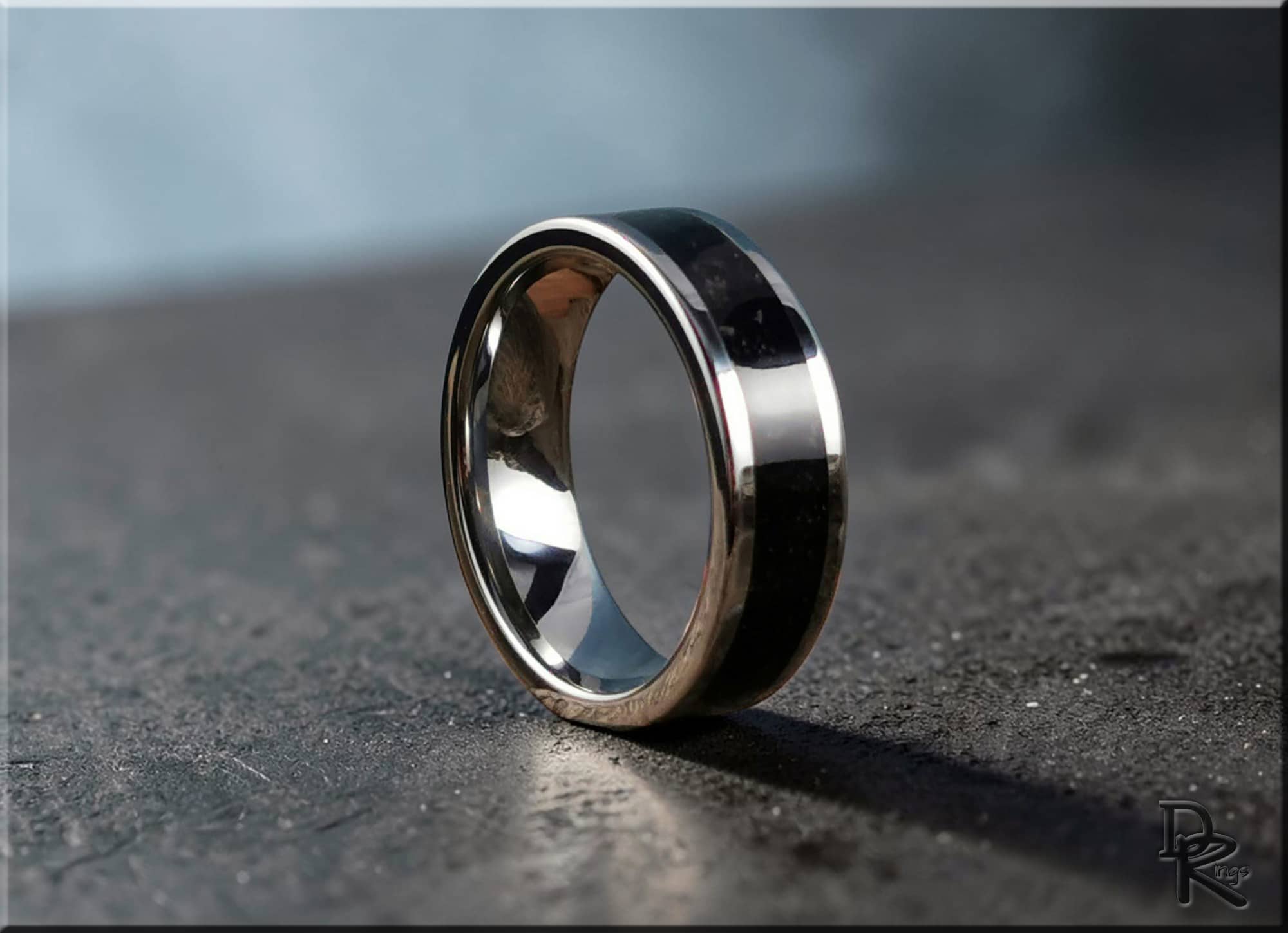 Tungsten ring with shungite featuring a polished silver edge and black stone center on textured surface