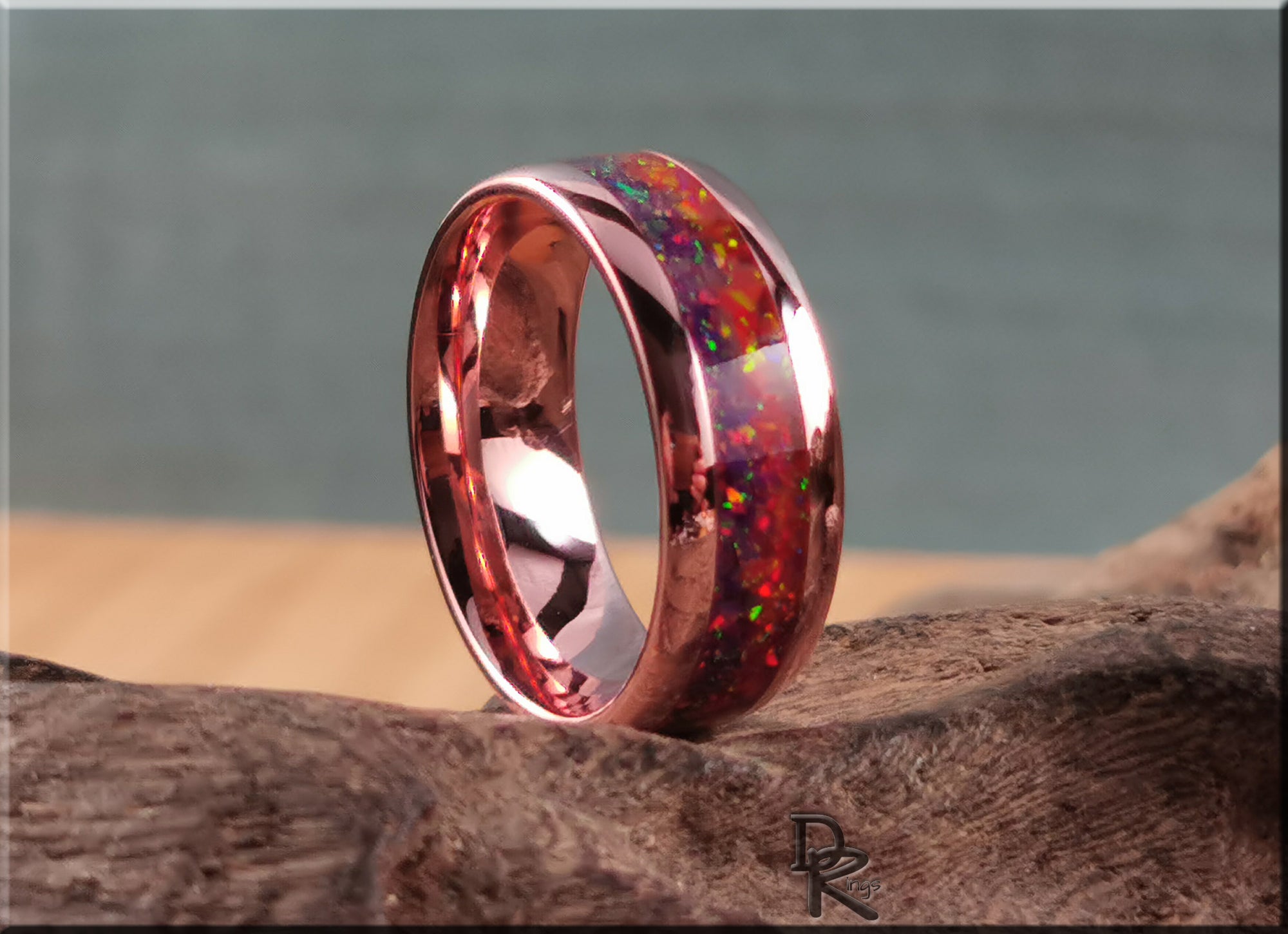 Brushed tellurium copper ring with opal featuring vibrant red and multicolor inlay on wooden surface