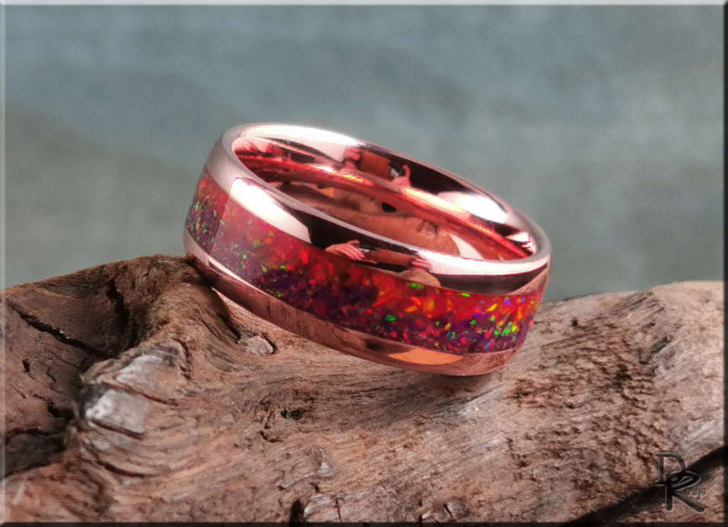 Brushed tellurium copper ring with opal inlay featuring vibrant red and multicolor flashes on a textured wood surface