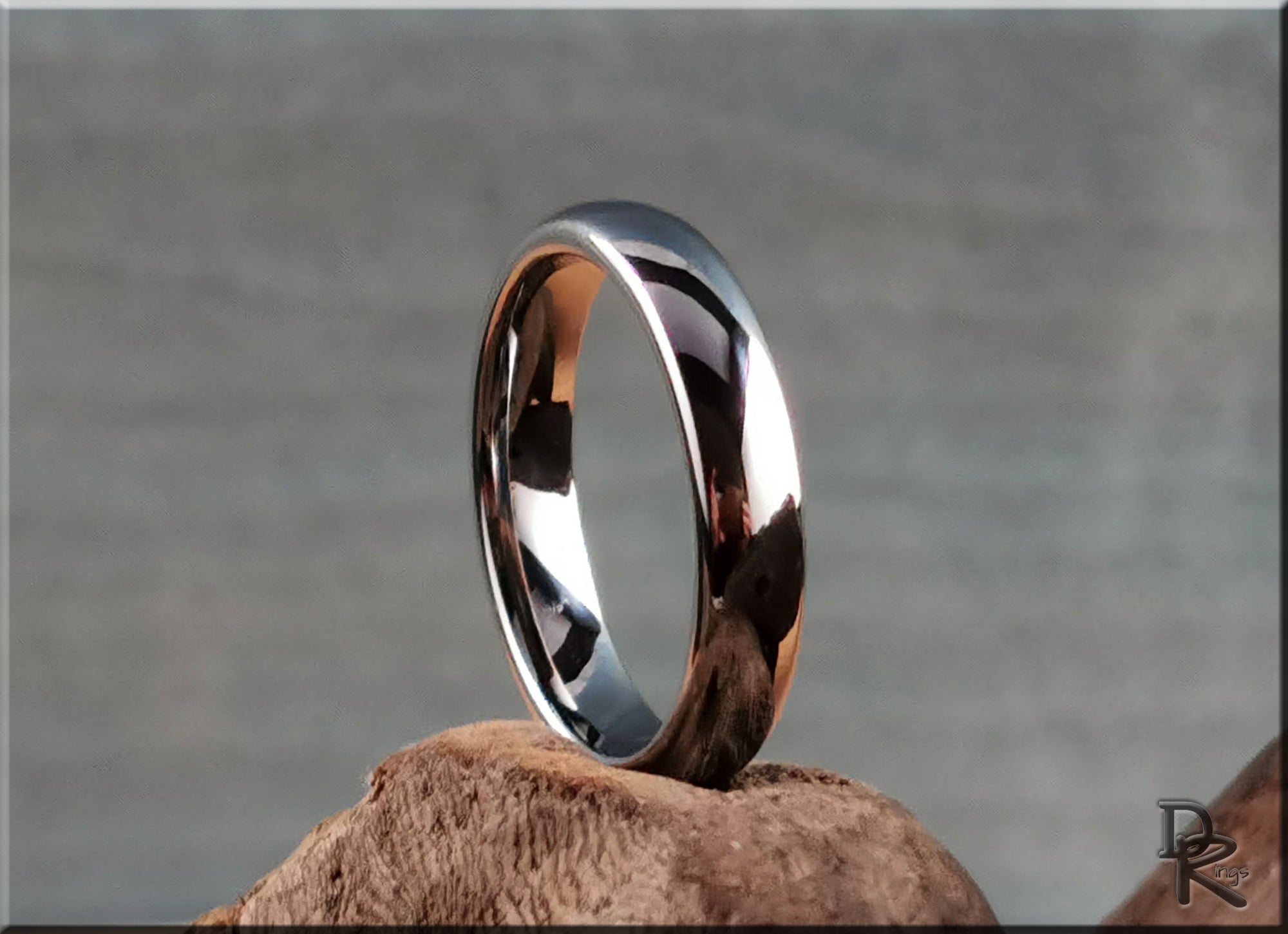 DR Rings polished domed tungsten ring with smooth reflective surface displayed on brown textured stone