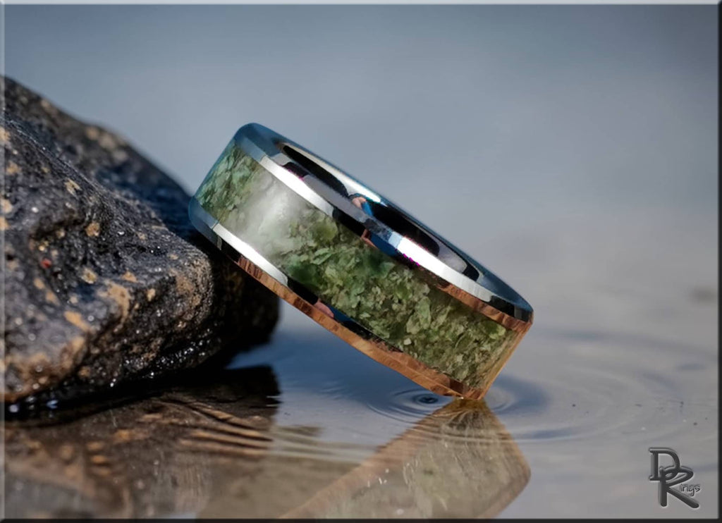 DR Rings tungsten ring with jade green inlay resting on a rock near water with reflections