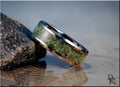 DR Rings tungsten ring with jade green inlay resting on a rock near water with reflections