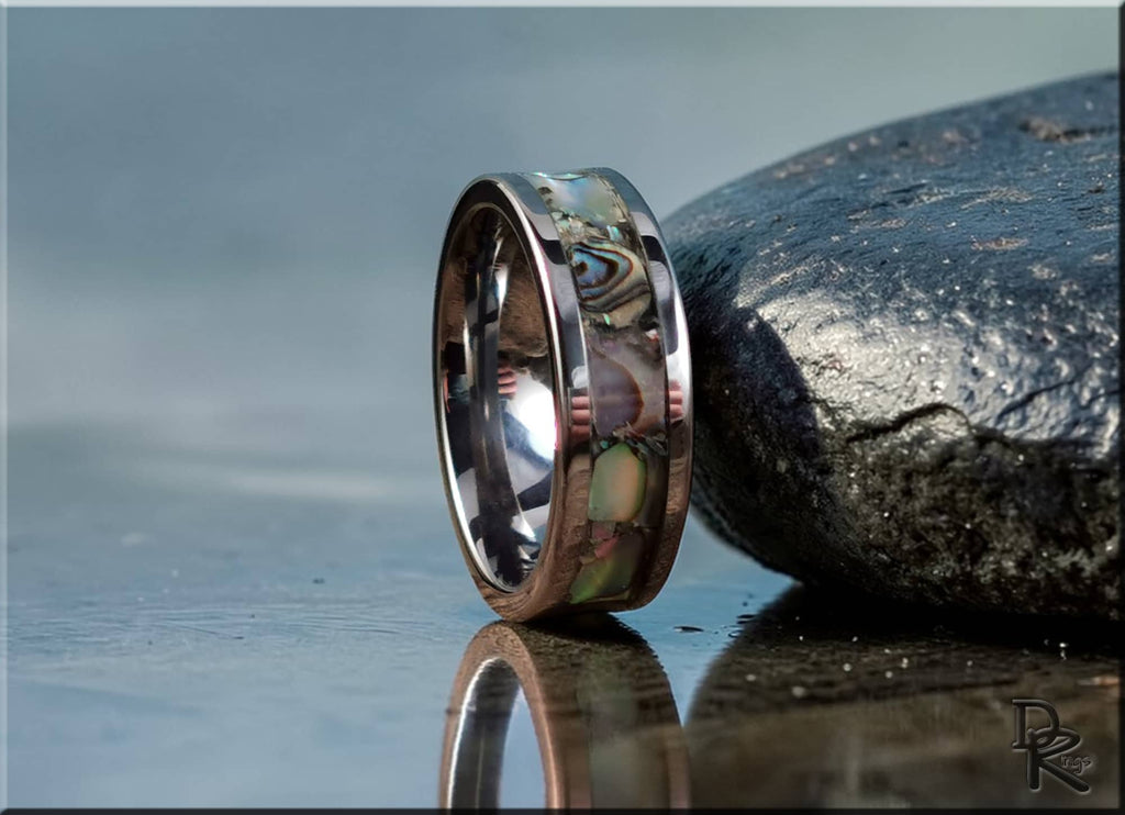 DR Rings super titanium ring with abalone shell inlay reflecting on a wet surface next to black stone