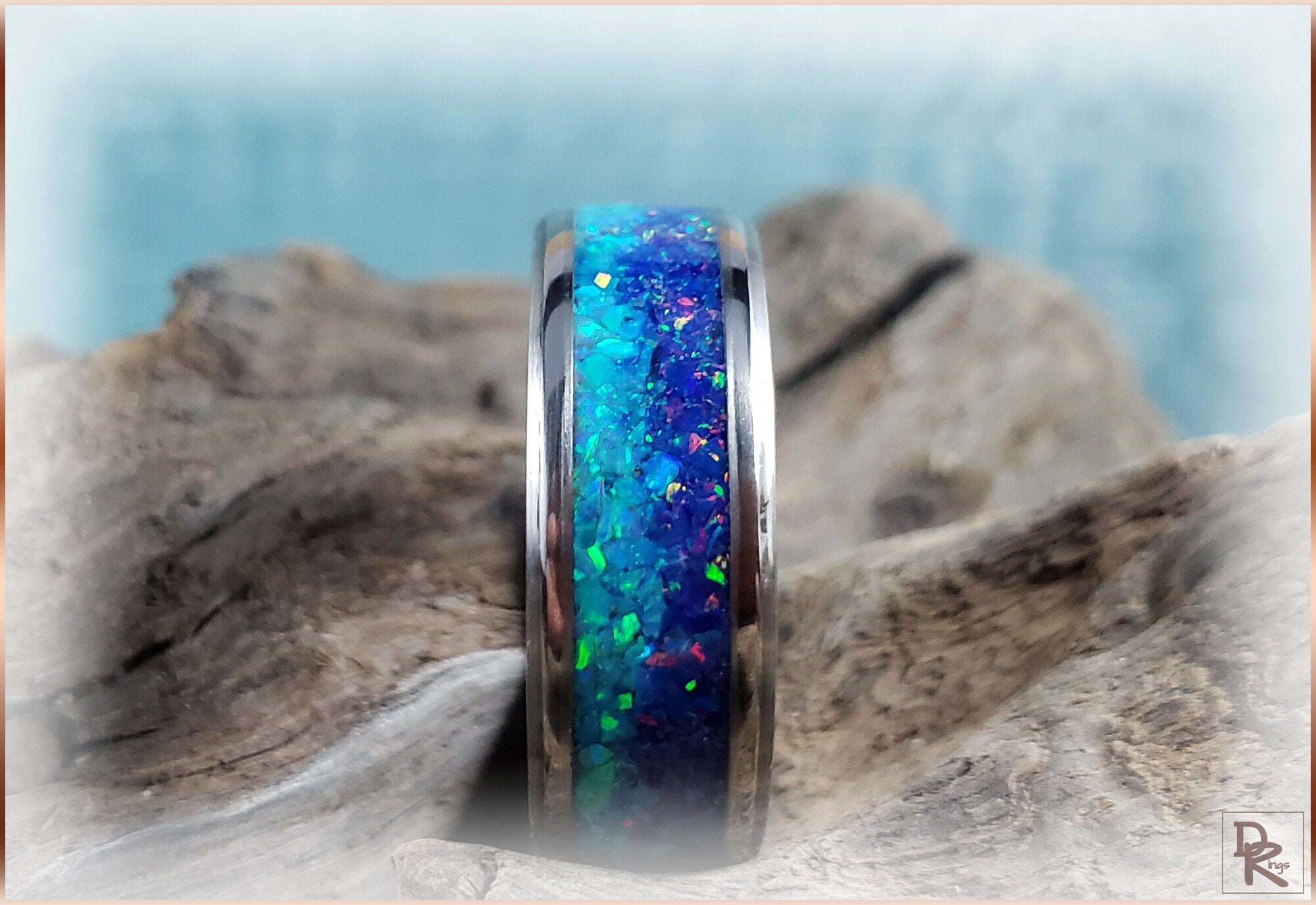 Titanium ring with opal inlay showing vibrant blue and green colors on a rustic wooden surface