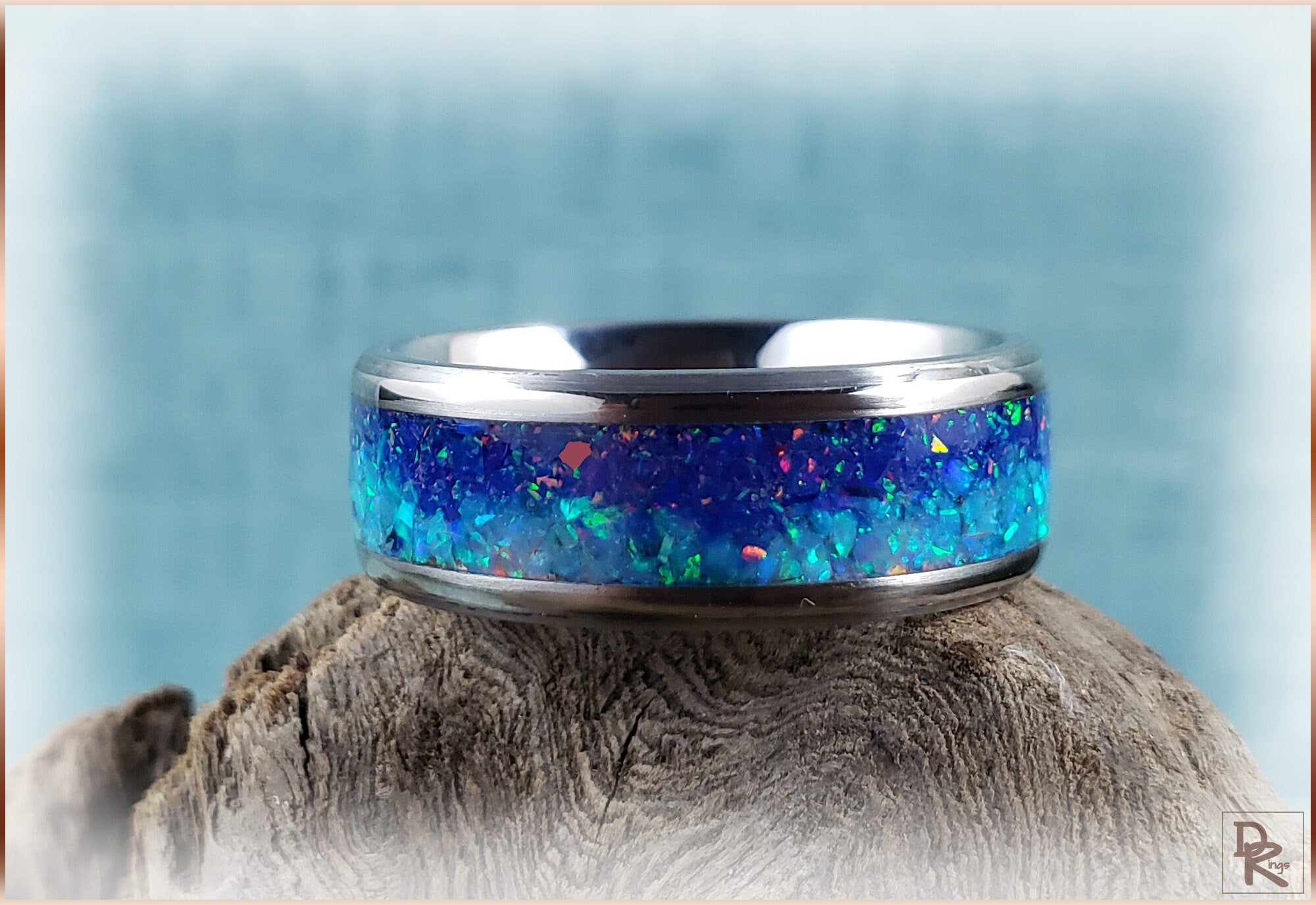 Titanium ring with opal inlay featuring vibrant blue and green colors on rustic wood background
