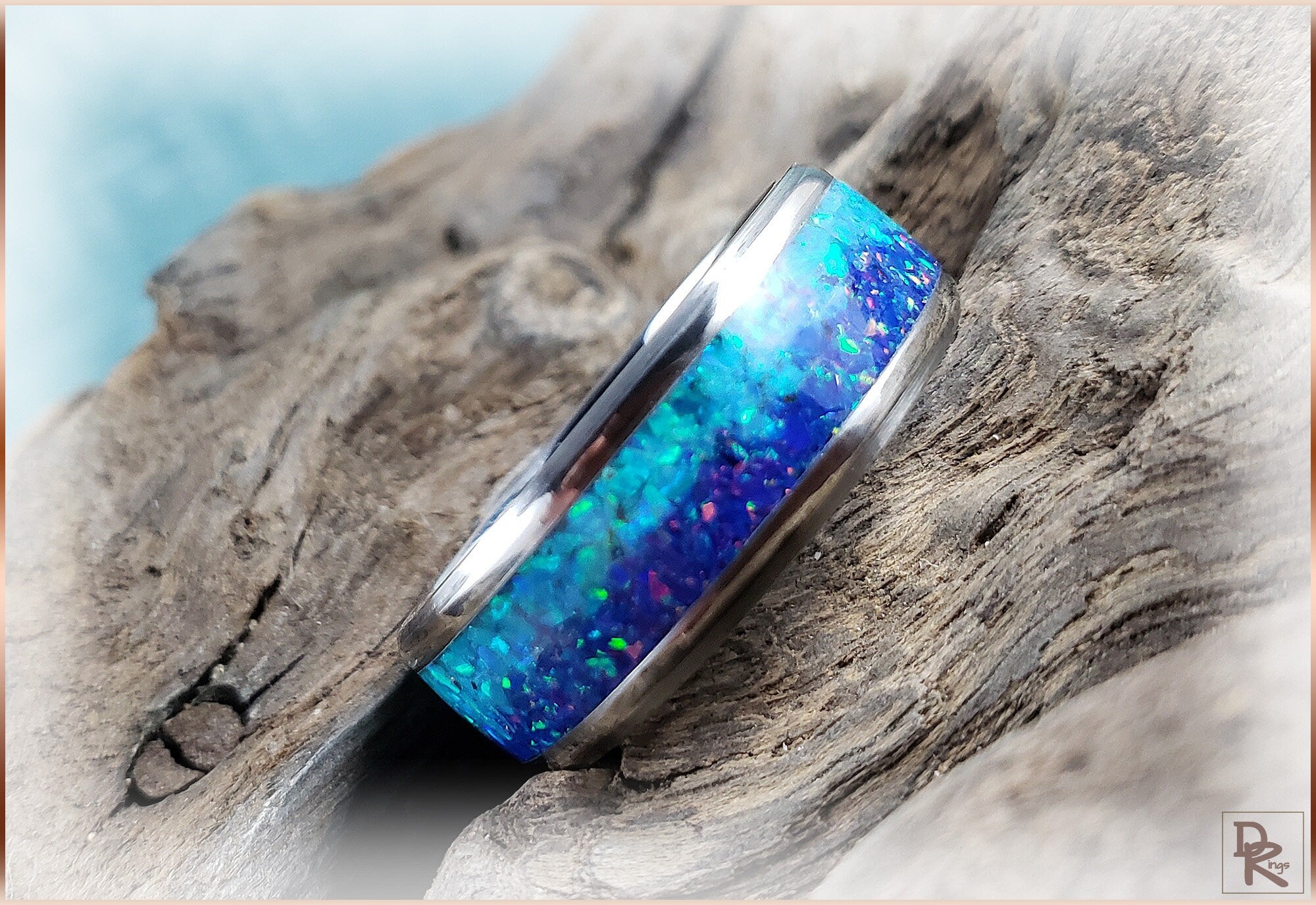 DR Rings titanium ring with opal inlay featuring vibrant blue and green colors on rustic wood background