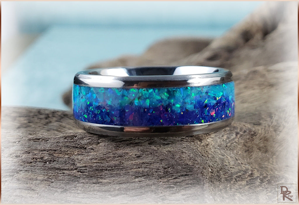 DR Rings titanium ring with opal inlay featuring vibrant blue and green colors on a rustic wooden surface