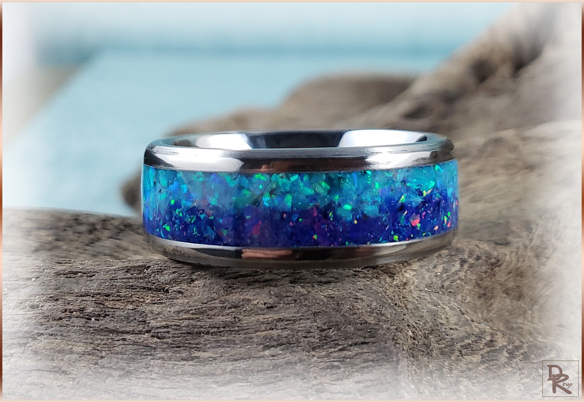 DR Rings titanium ring with opal inlay featuring vibrant blue and green colors on a rustic wooden surface