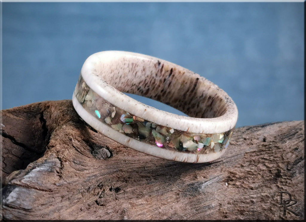 DR Rings antler ring with abalone inlay resting on rustic wood with blue background