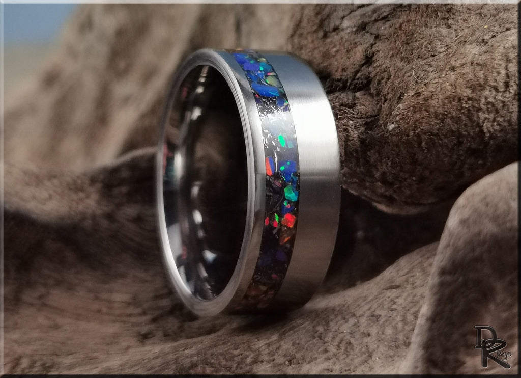 DR Rings titanium ring with meteorite inlay featuring colorful opal design on a textured background