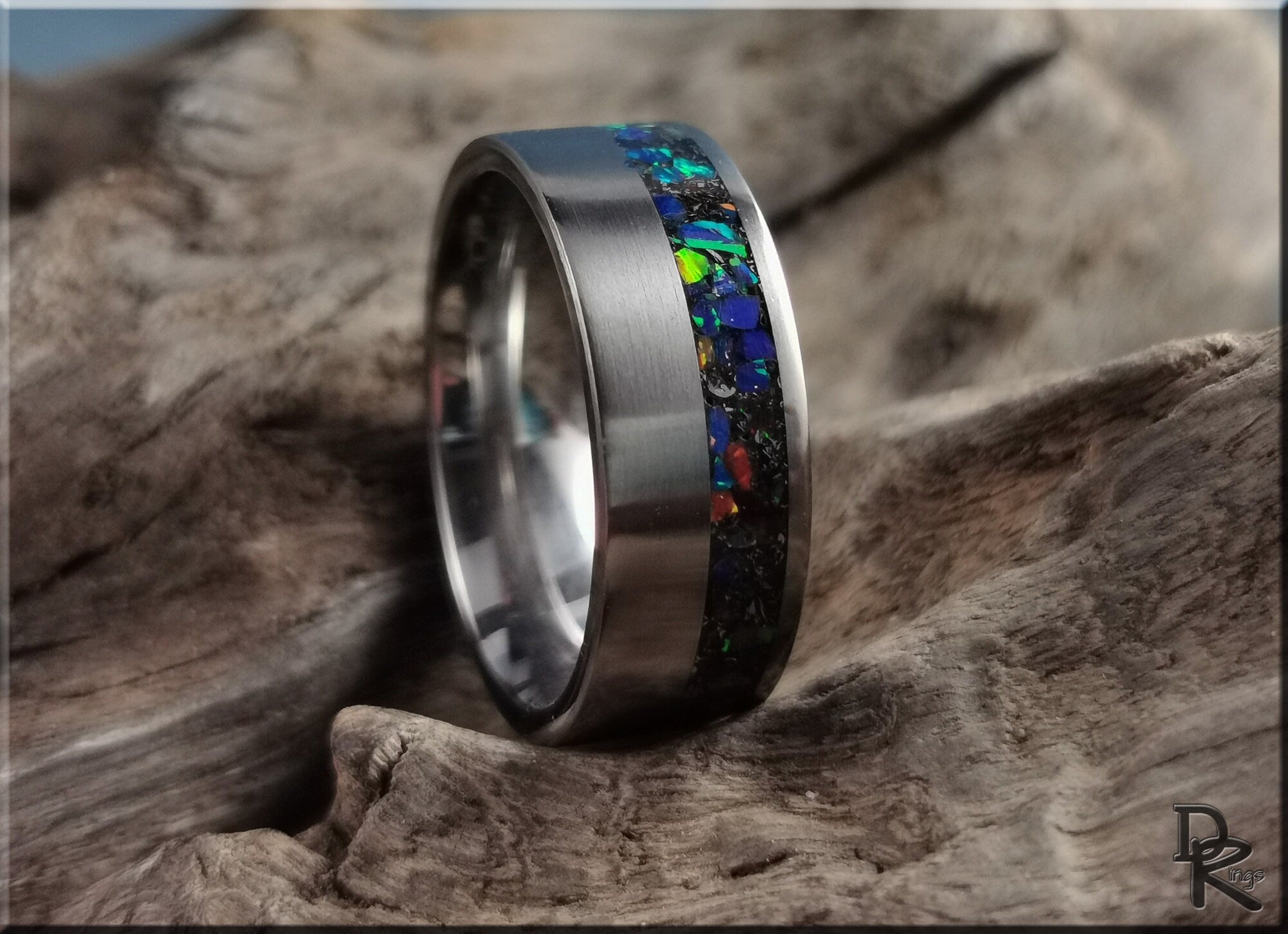 DR Rings titanium ring with meteorite inlay featuring colorful gemstone accents on wood background