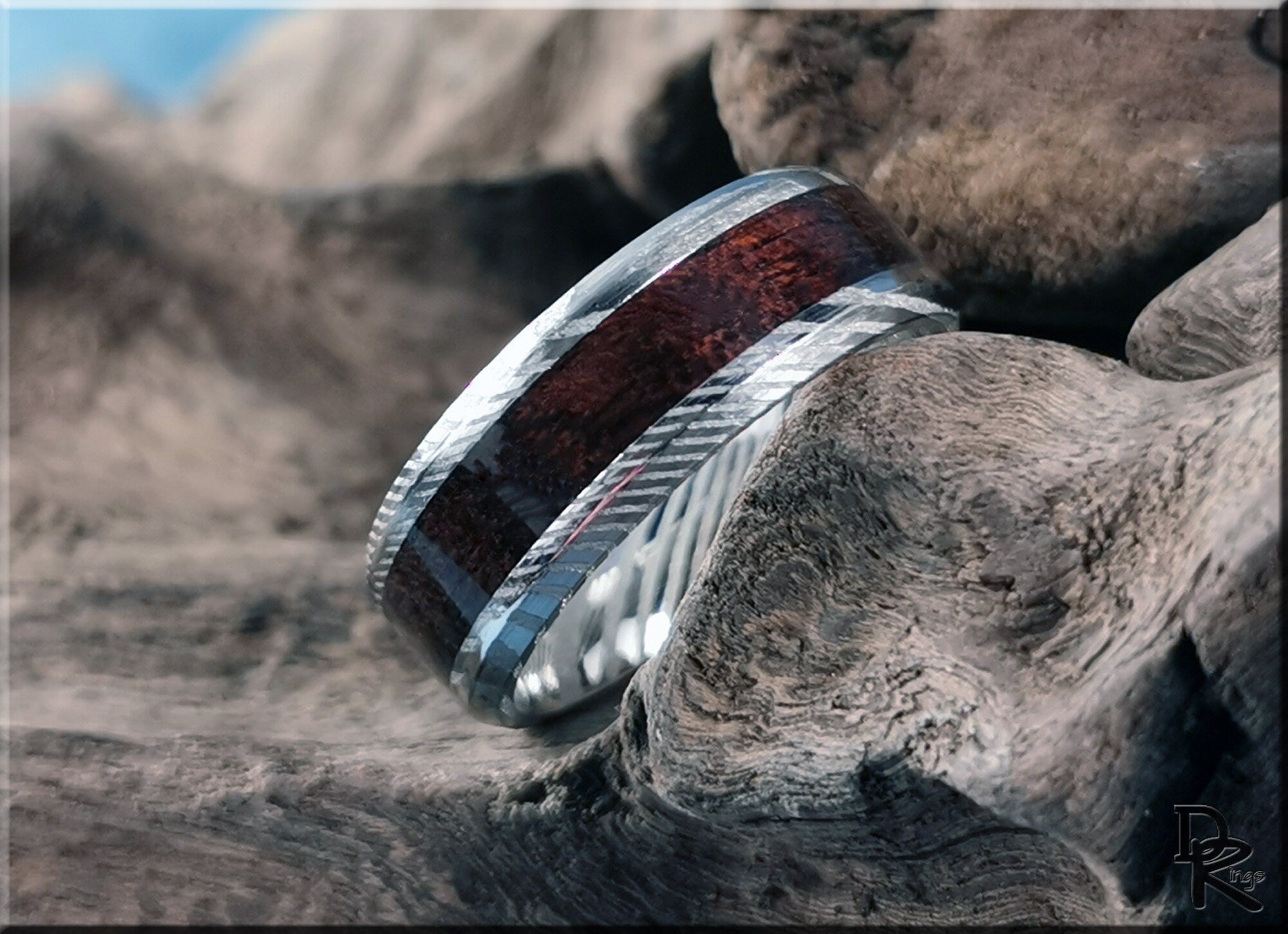 Damascus steel ring with wood inlay featuring textured silver edges resting on natural wood