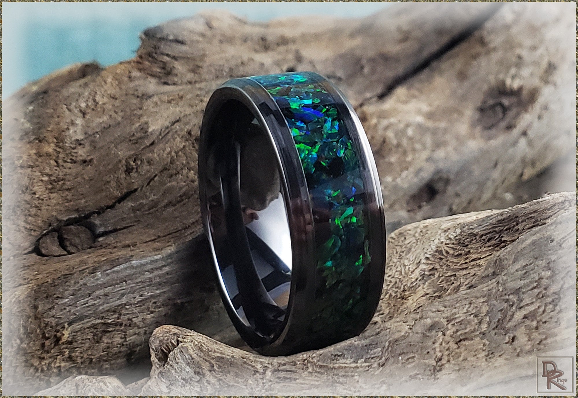 DR Rings black ceramic ring with blue and green inlay resting on natural driftwood
