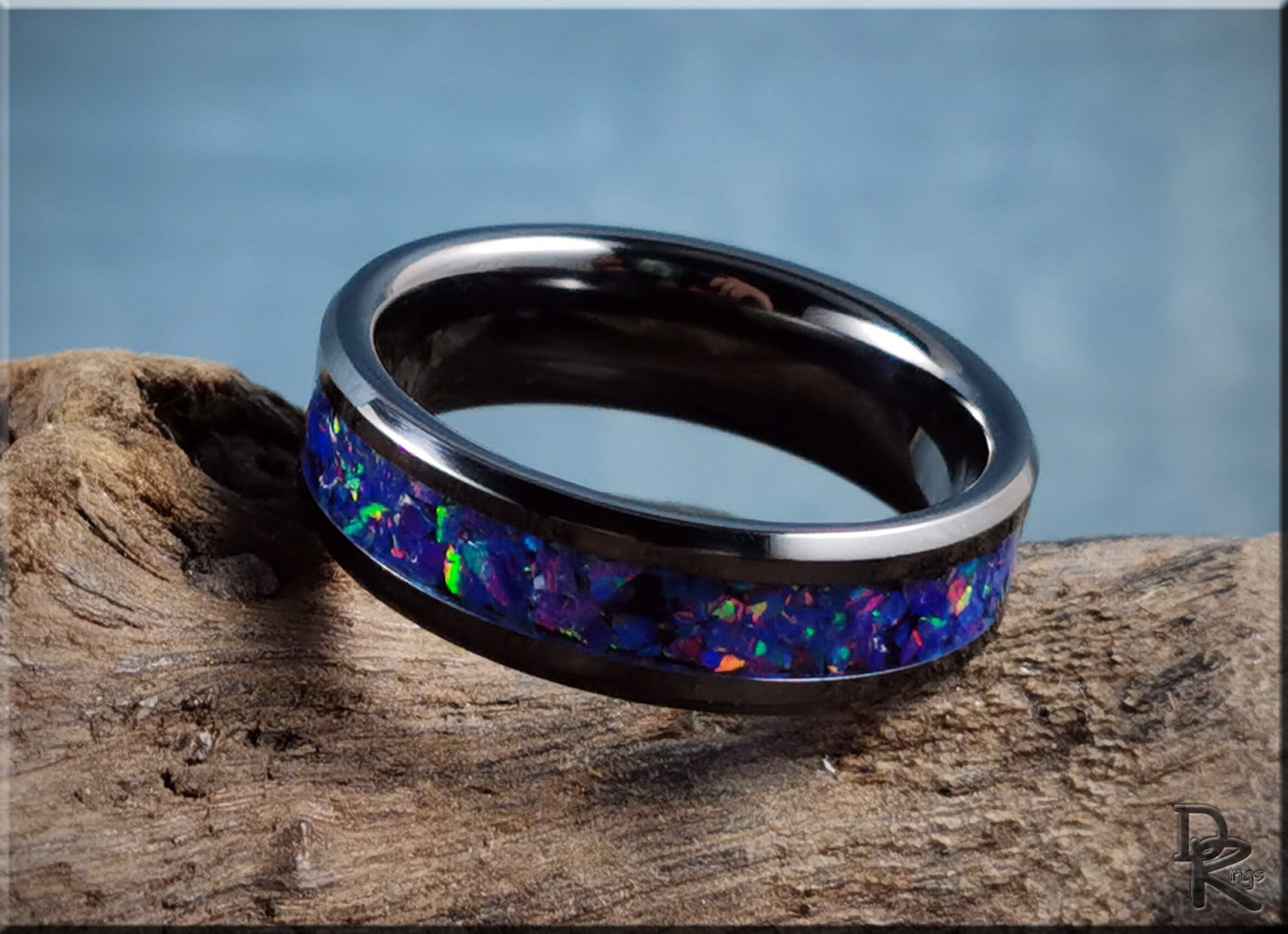 Ceramic ring with inlay featuring vibrant blue and purple opal stones on natural wood background