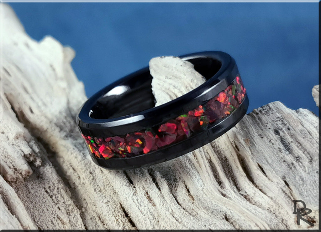 Black ceramic ring with inlay of red and orange stones on textured wood background by DR Rings