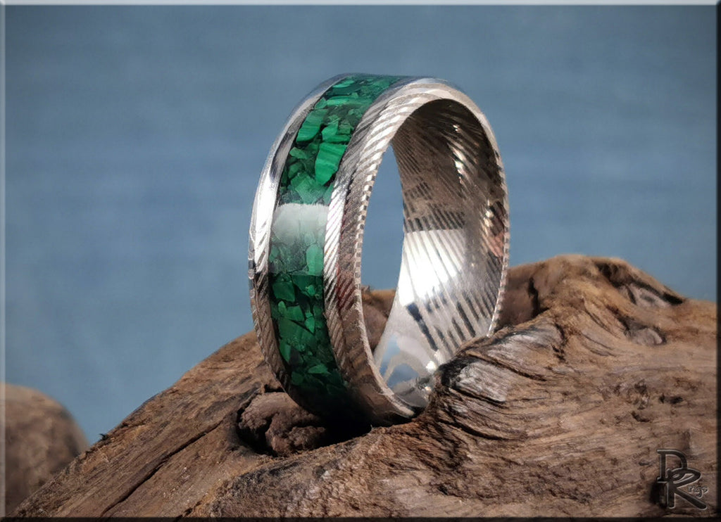 Damascus steel ring with malachite inlay featuring a polished silver finish on rustic wood