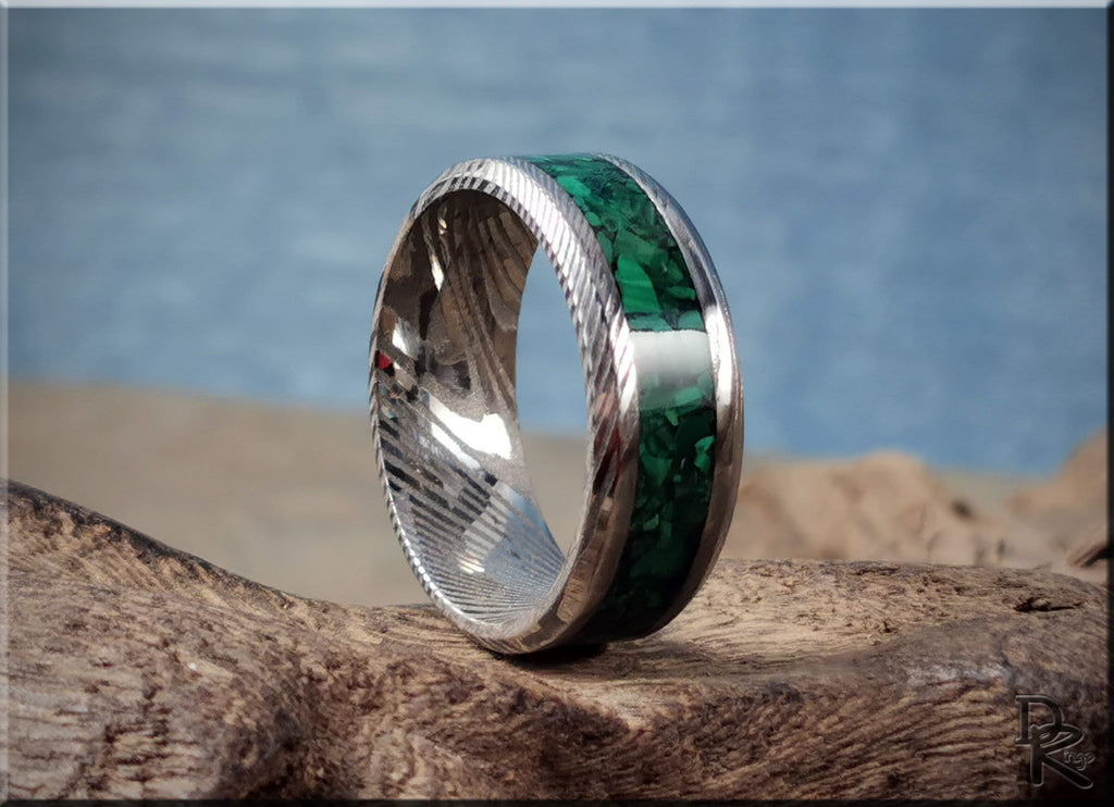 Damascus steel ring with malachite green inlay by DR Rings displayed on rustic wood background
