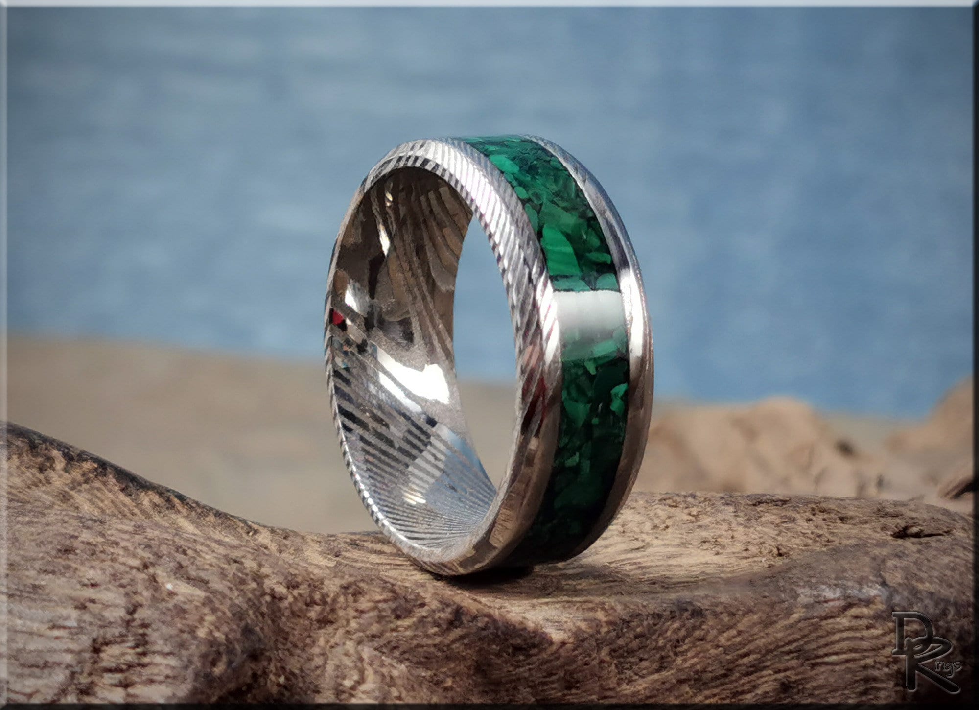 Damascus steel ring with malachite green inlay by DR Rings displayed on rustic wood background