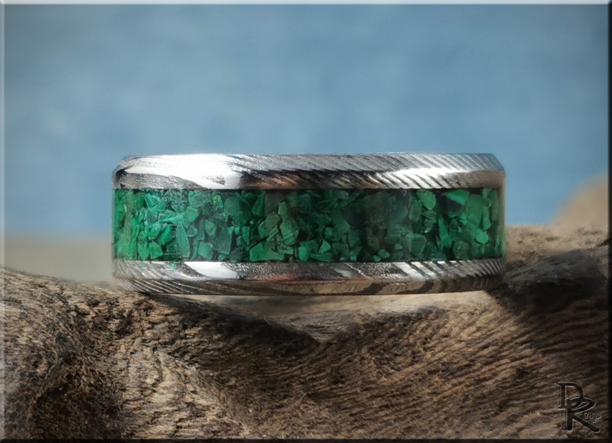 Damascus steel ring with malachite inlay by DR Rings displayed on textured wood