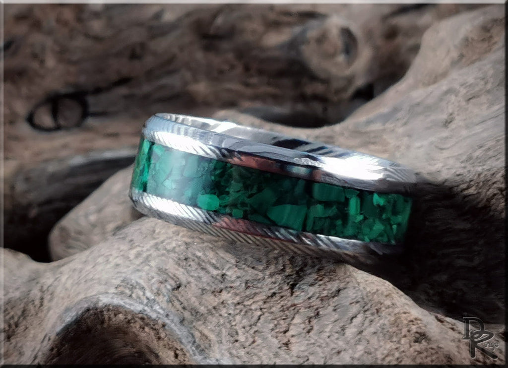 Damascus steel ring with malachite green stone inlay by DR Rings on textured wood background