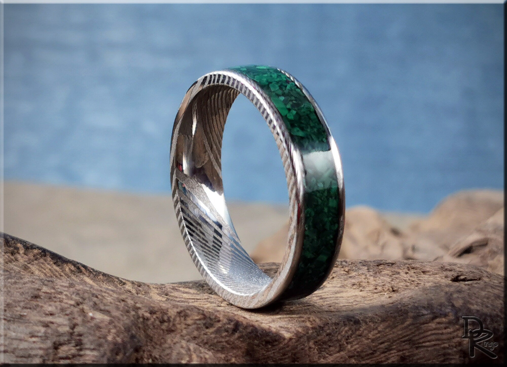 Damascus steel ring with malachite inlay shown on natural wood surface with blue background