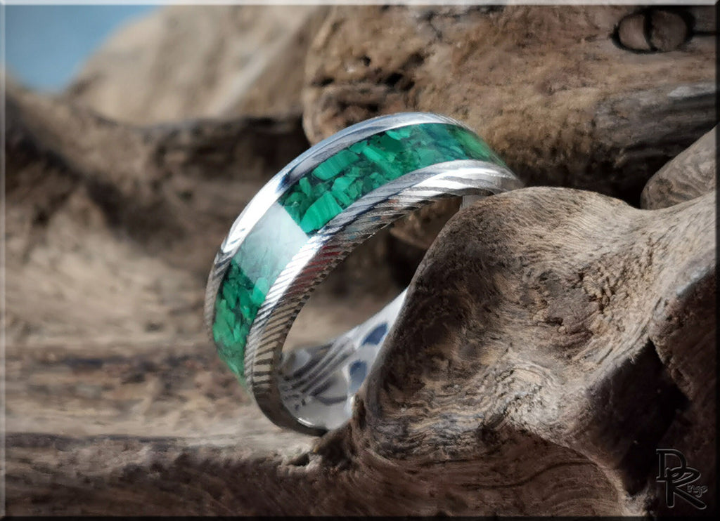 Damascus steel ring with malachite green stone inlay displayed on rustic wood background