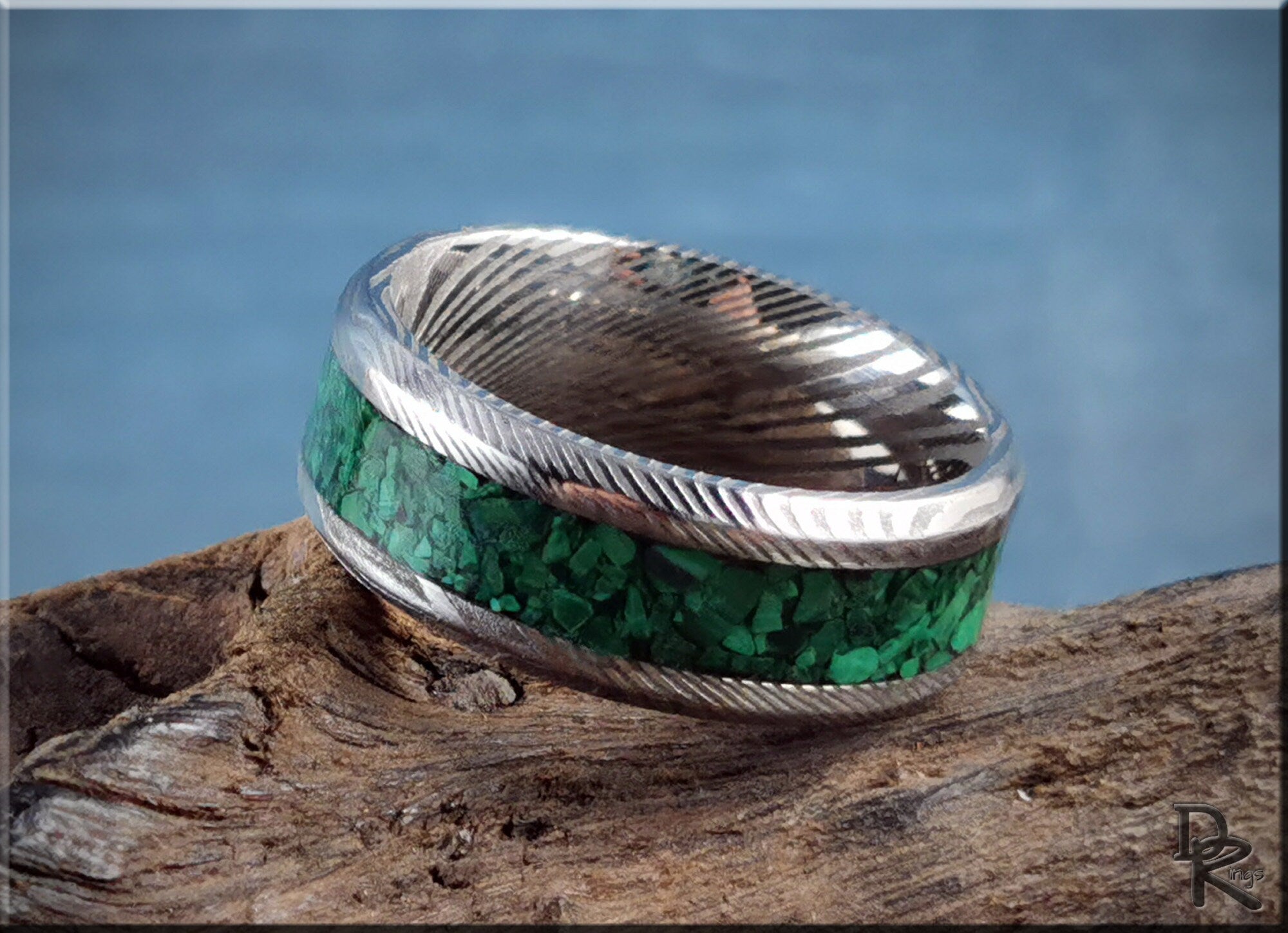 Damascus steel ring with malachite inlay featuring intricate textured edges on rustic wood