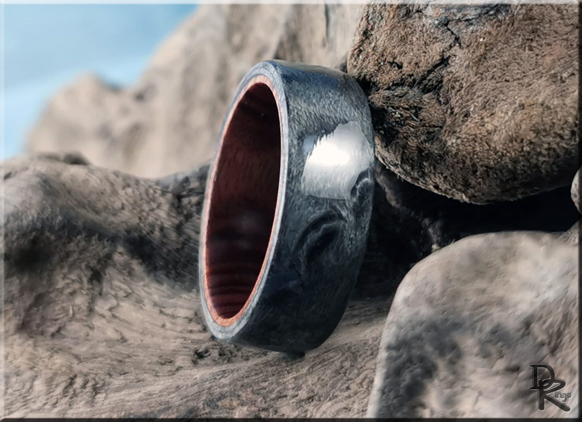 DR Rings grey maple ring with polished dark grey finish and wooden interior on natural rock background