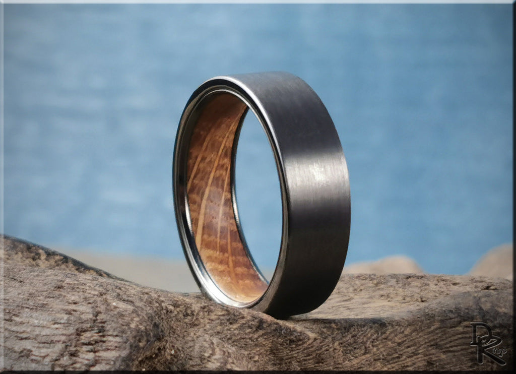 DR Rings gun metal tungsten ring with wood inlay on textured wooden surface against blue background