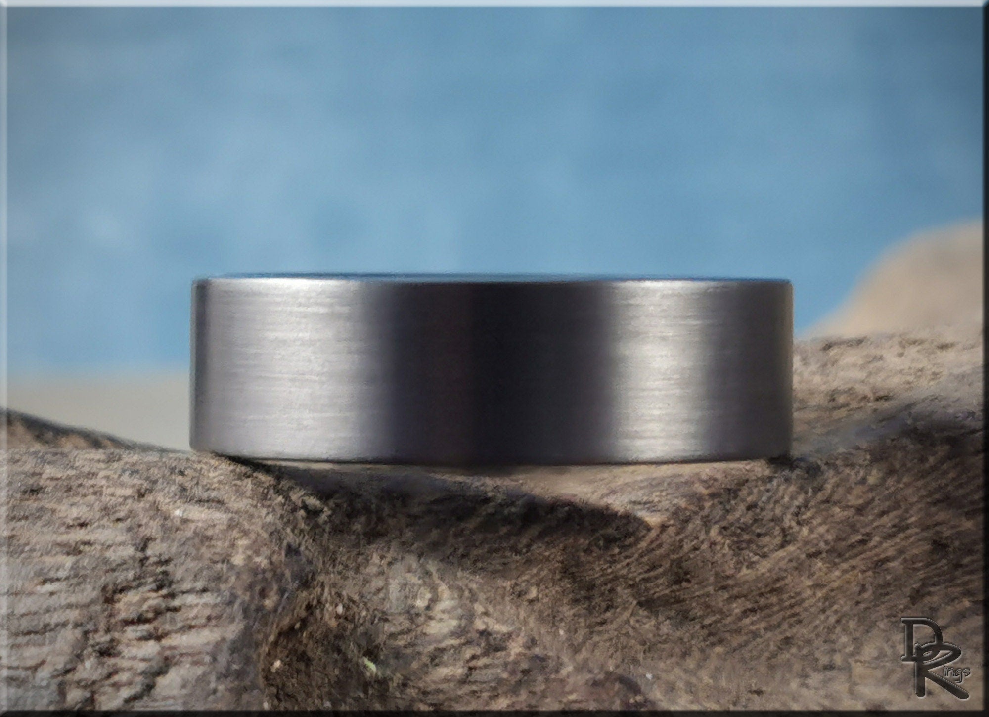 DR Rings gun metal tungsten ring with a smooth brushed finish on rustic wood background