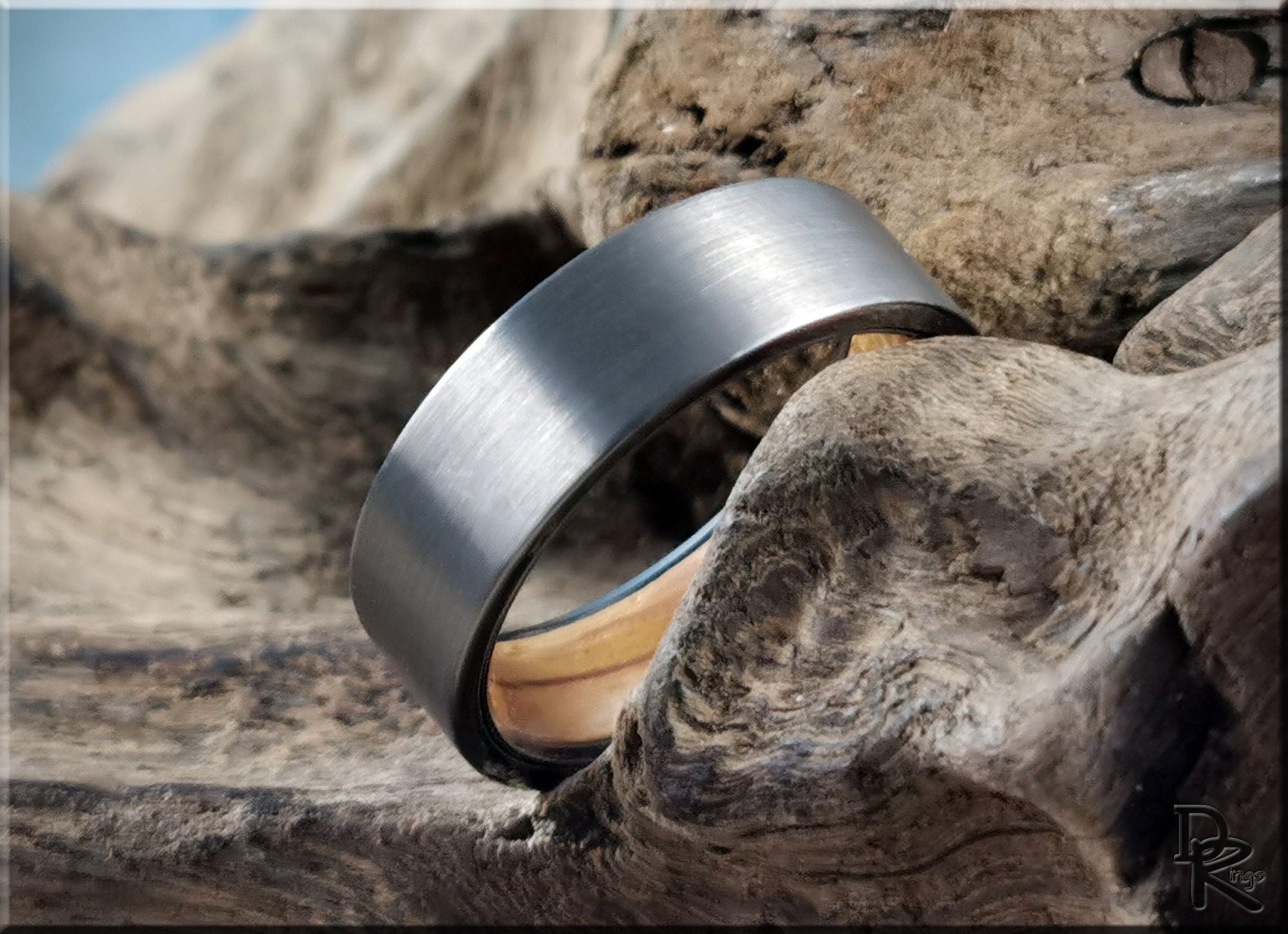 DR Rings gun metal tungsten ring with brushed finish resting on natural wood surface