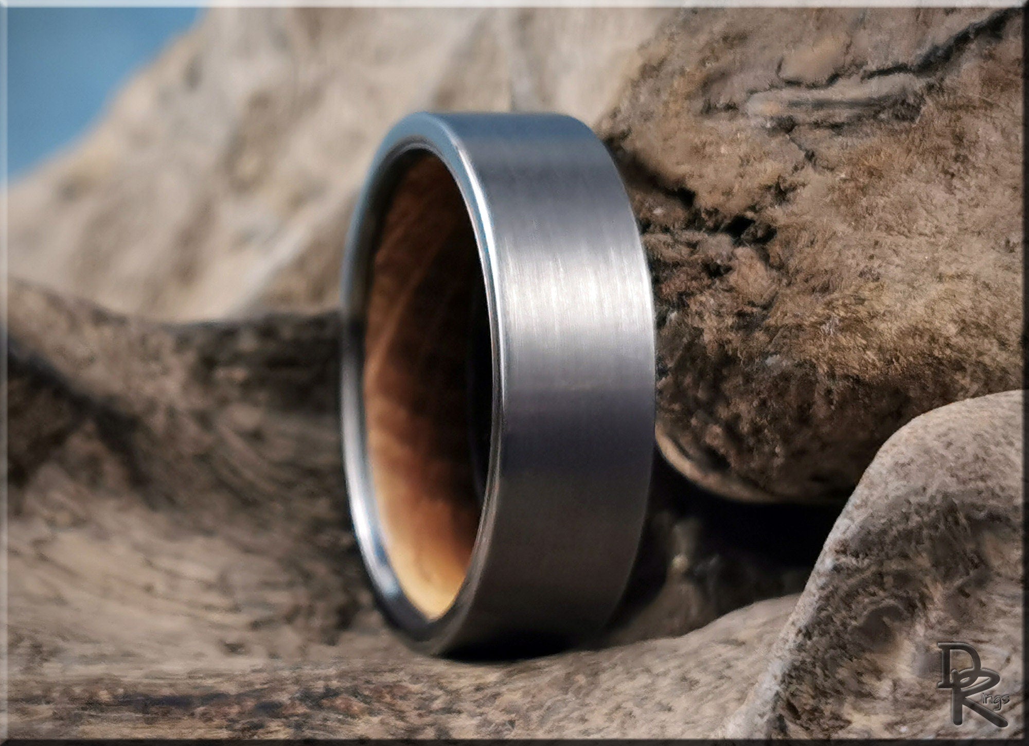 Gun metal tungsten ring with brushed finish and wooden interior by DR Rings on textured wood background
