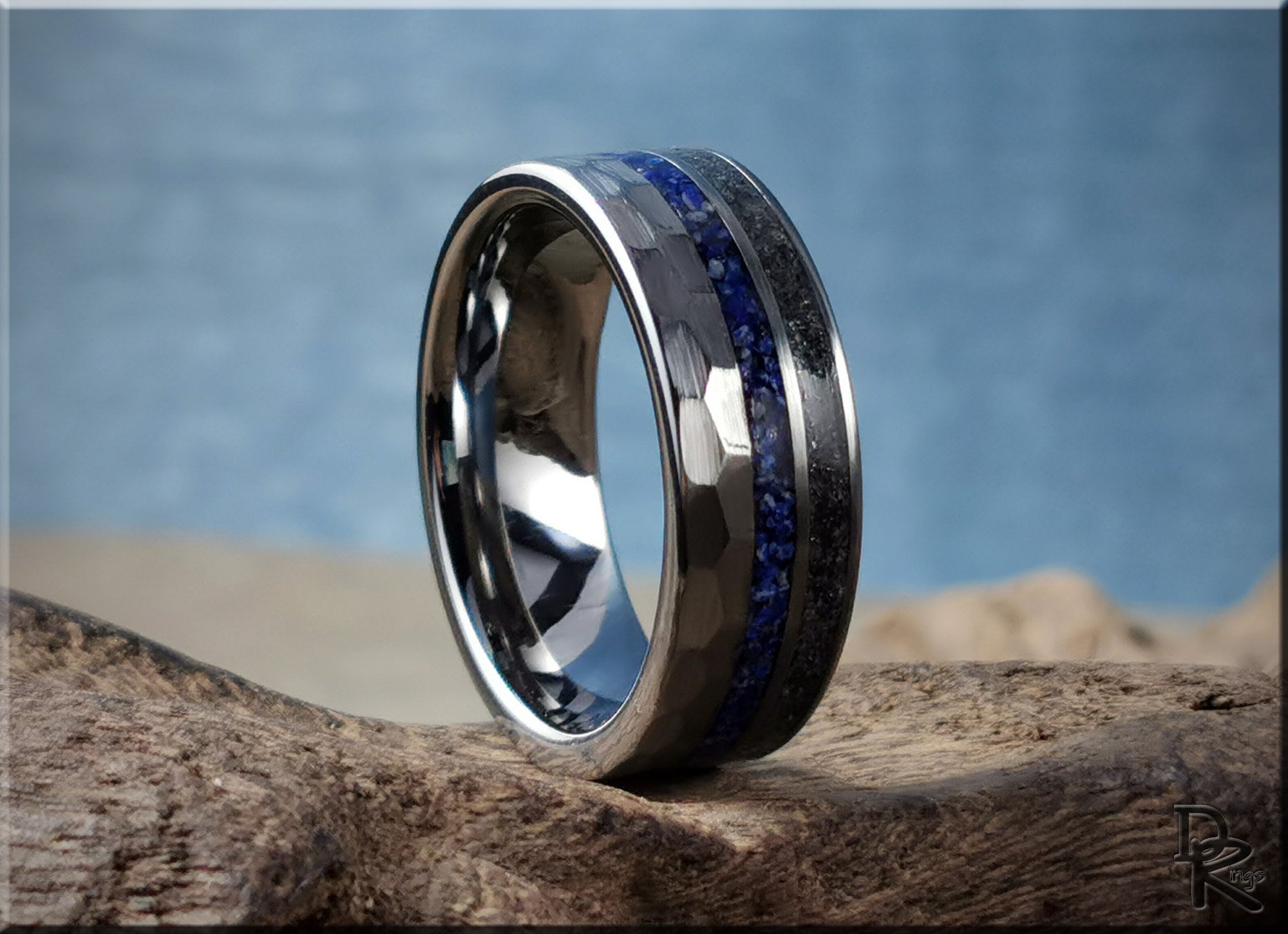 Hammered tungsten ring with two inlays featuring blue and black textured bands on wood surface